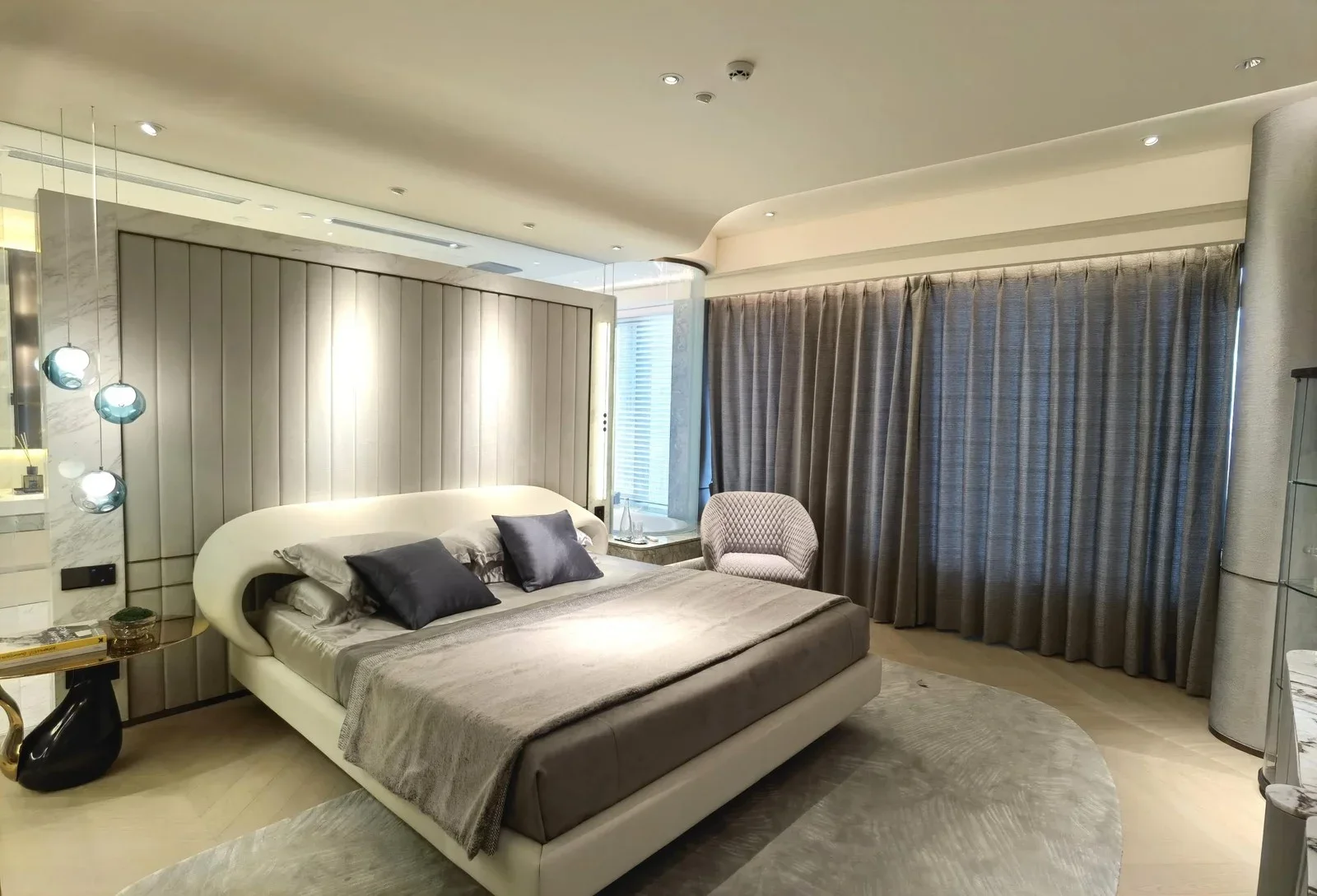 Suite bedroom with a curved upholstered bed, a tufted lounge chair and a padded wall
